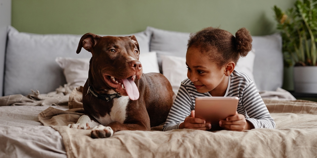 girl on a tablet laying in bed with a dog