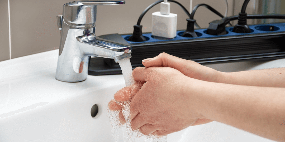 person washing hands next to power strip with lots of plugs