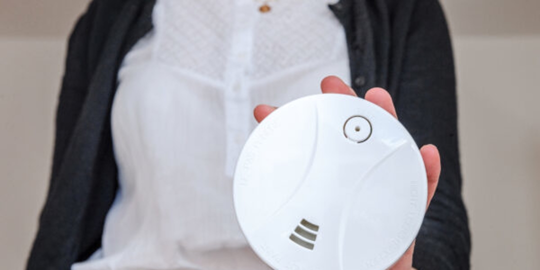 An image of a lady holding a carbon monoxide detector