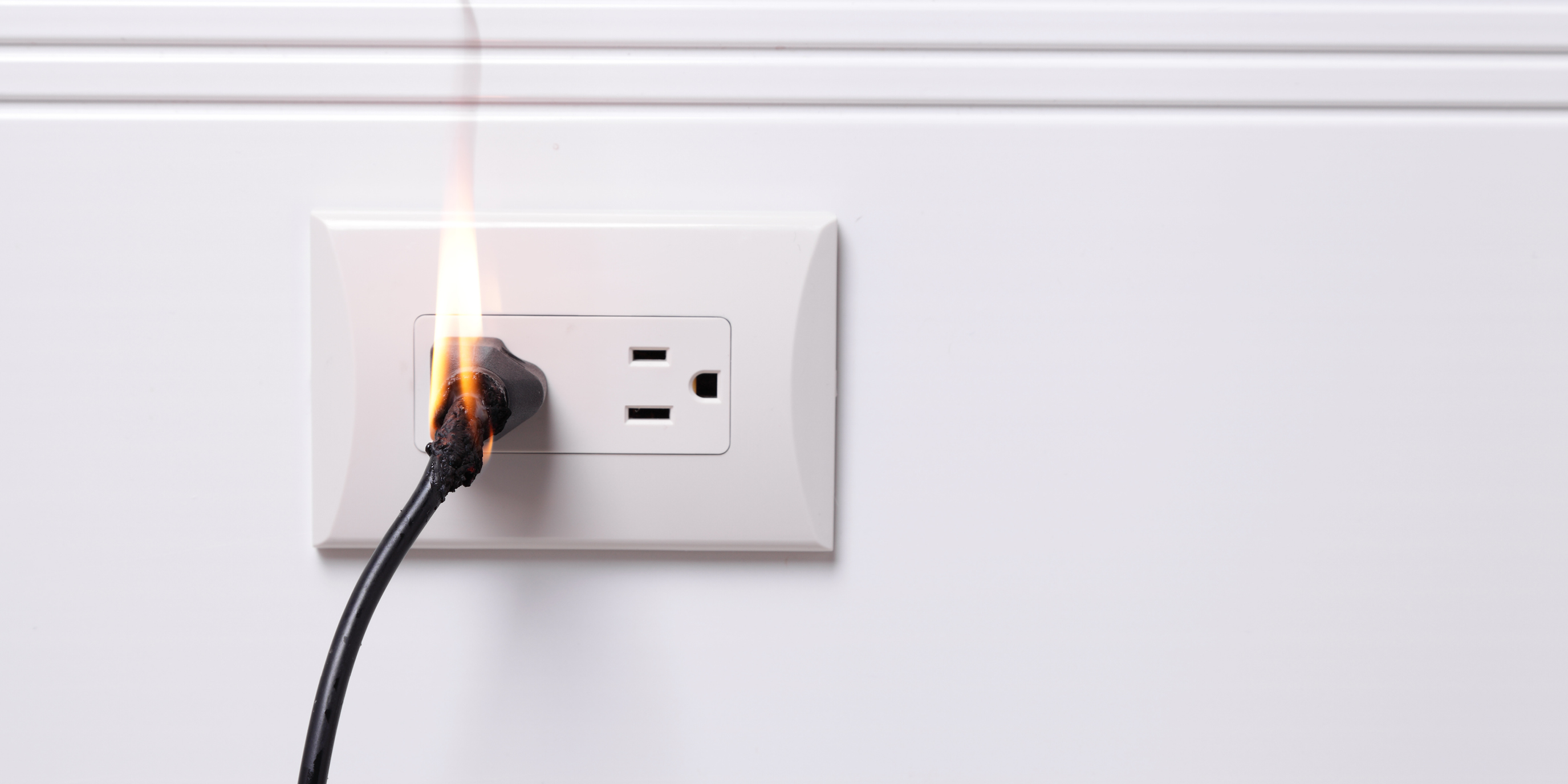 An electrical cord on fire in an outlet.