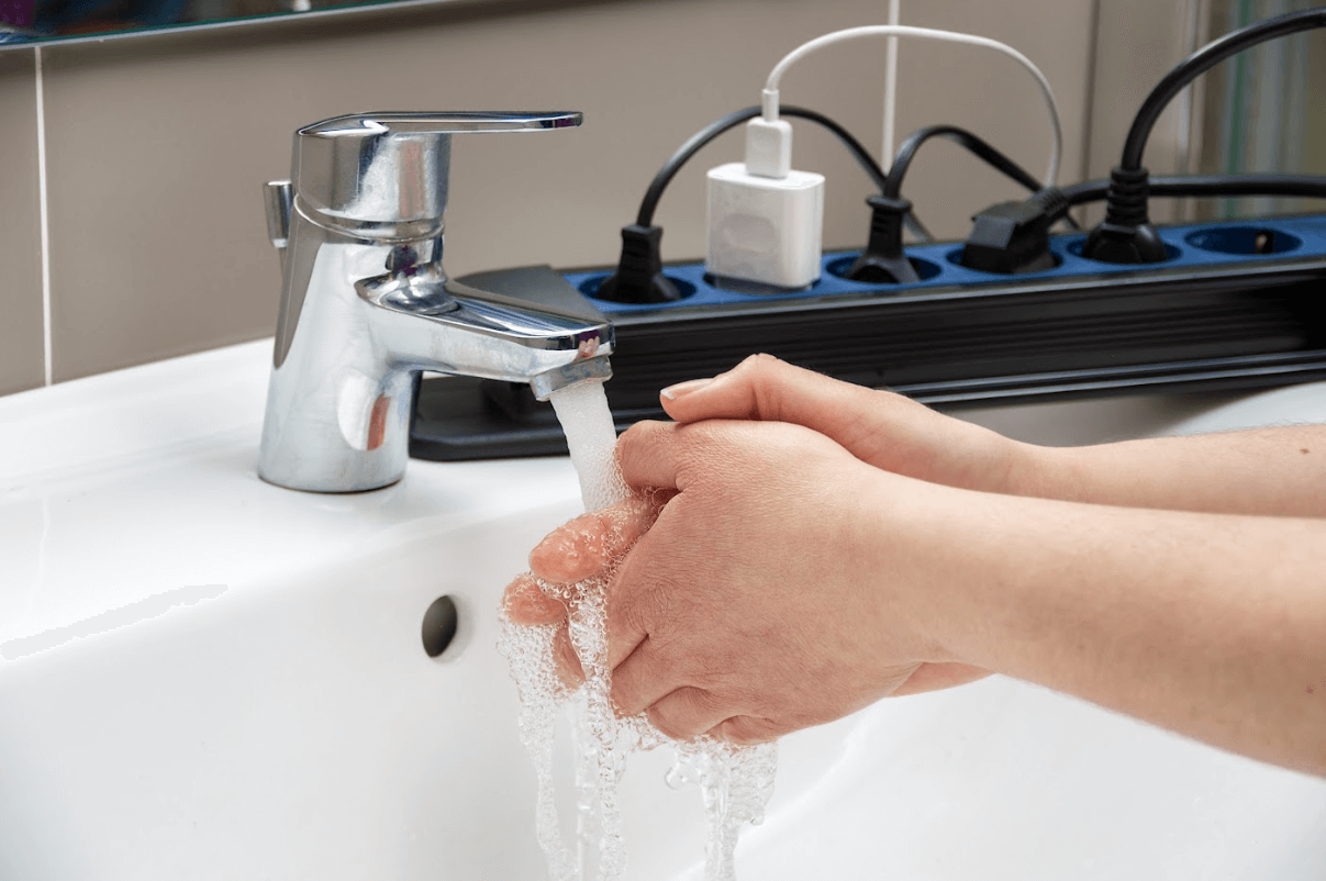 person washing hands next to power strip with lots of plugs