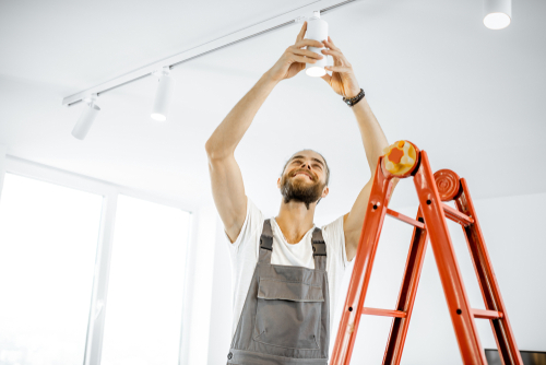 electrician replacing track lighting on a ceiling standing on a ladder